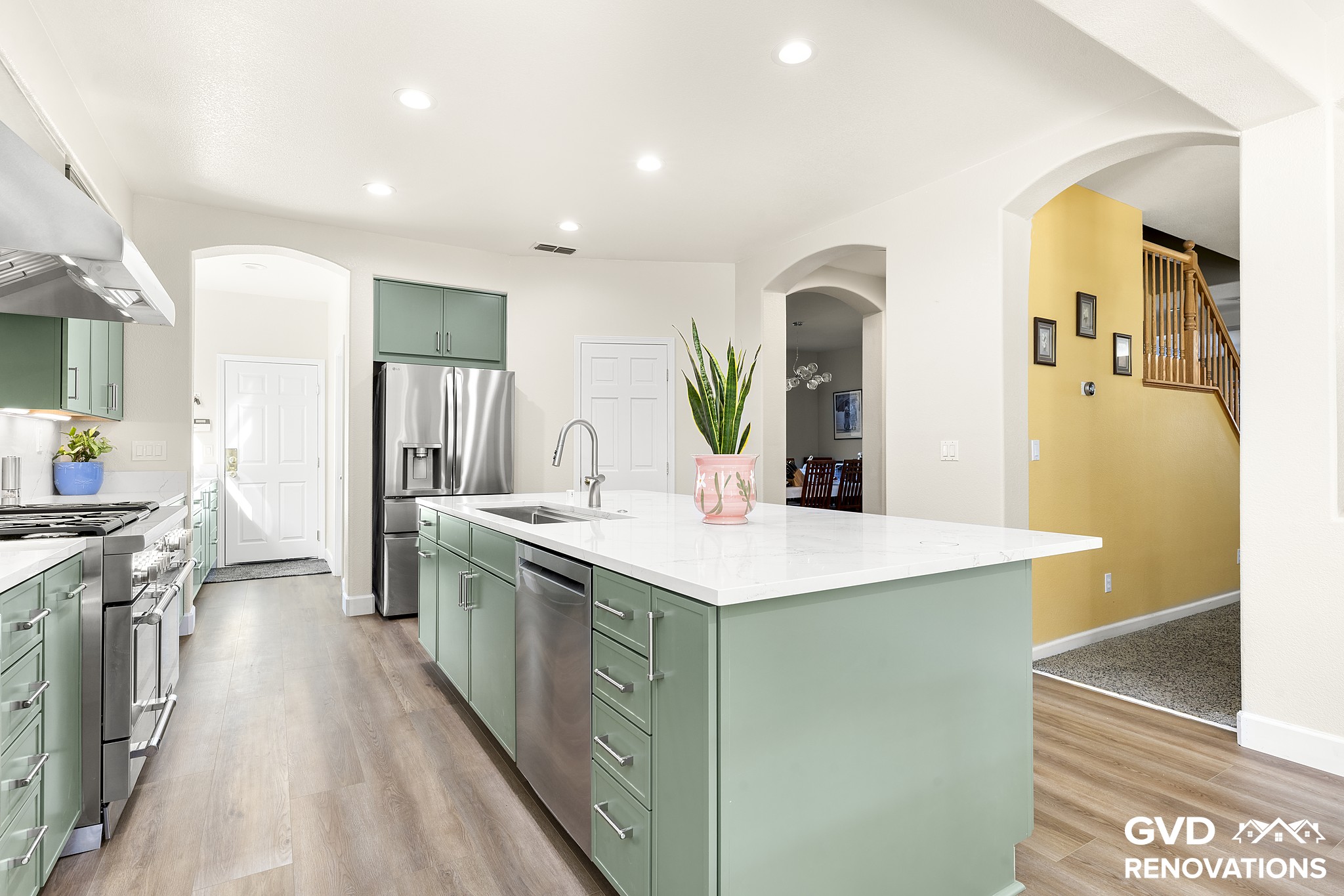 Wide view of the remodeled kitchen from the dining area with green cabinets, a quartz island and stainless steel appliances