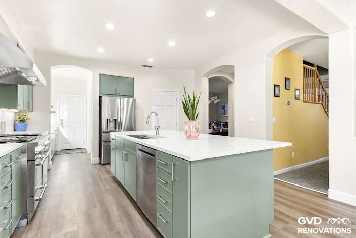 Wide view of the remodeled kitchen from the dining area with green cabinets, a quartz island and stainless steel appliances