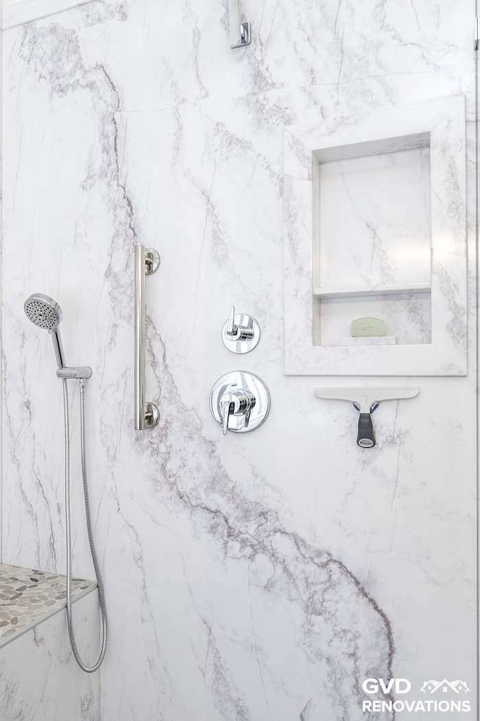 Recessed shower niche and tiled shelf with a handheld sprayer in marble-look tile