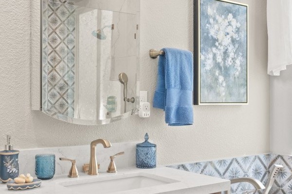 Bathroom vanity and drop-in tub beneath a window with marble-look tile and a blue accent band