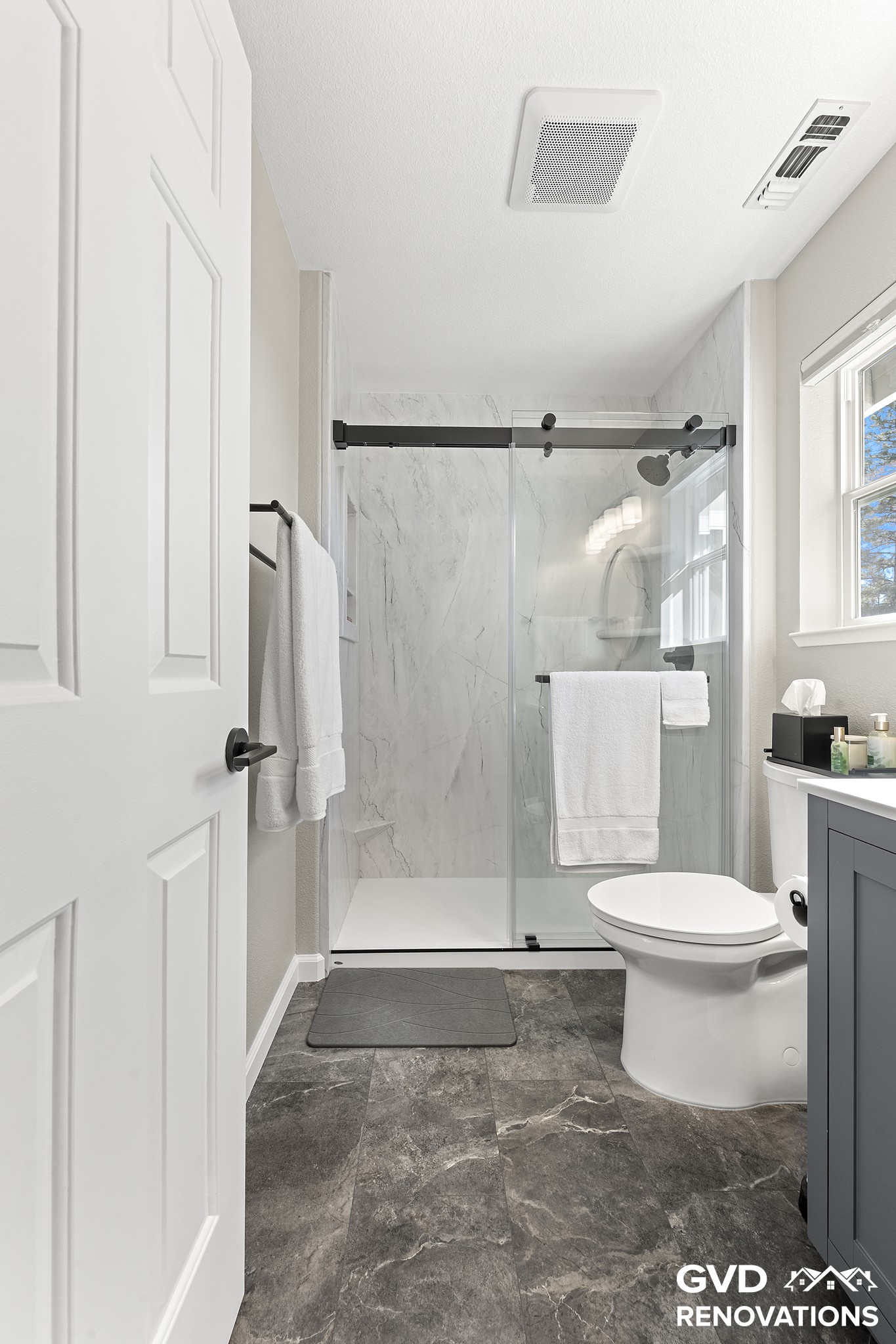 Hall bath with a grey vanity and a marble-look walk-in shower behind a sliding glass door