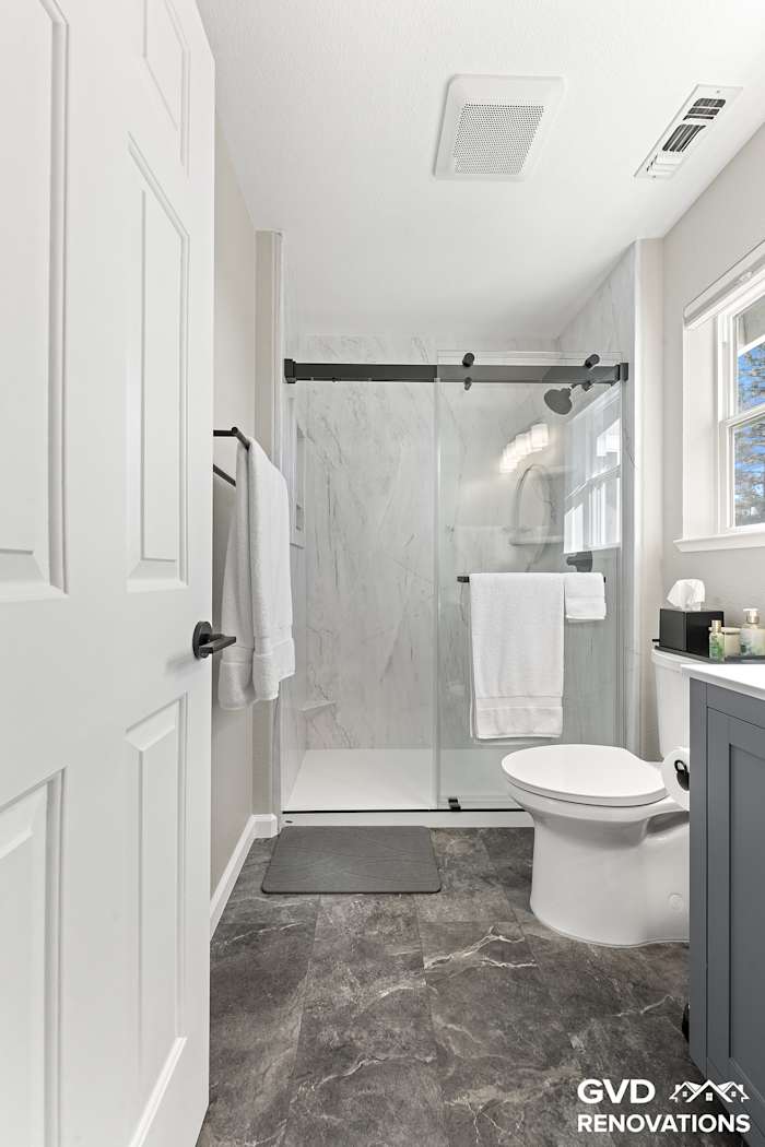 Hall bath with a grey vanity and a marble-look walk-in shower behind a sliding glass door