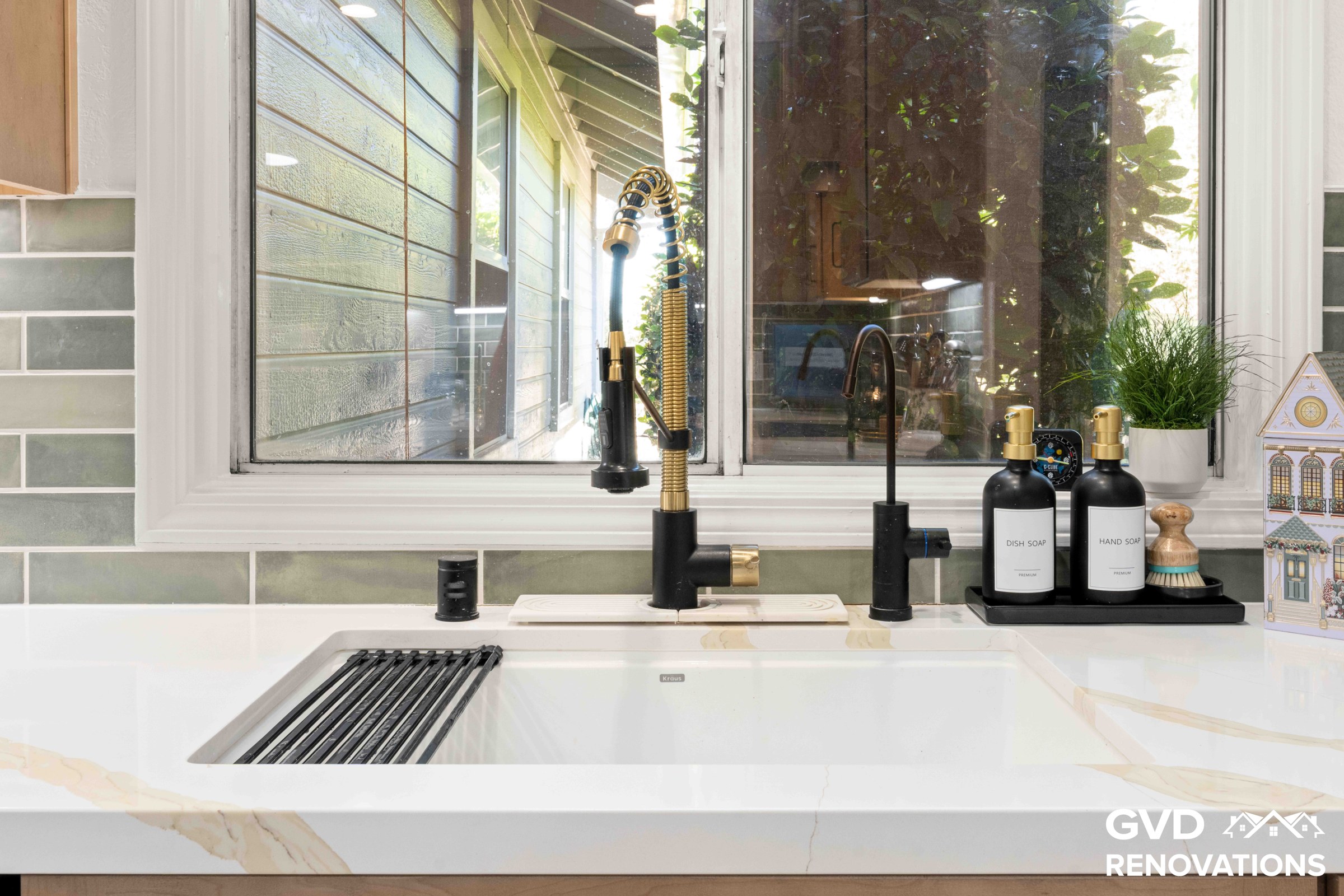 Close-up of the kitchen sink with a black and brass spring-neck faucet and roll-up drying rack beneath a garden window