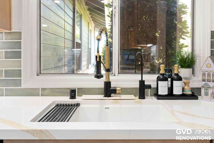 Close-up of the kitchen sink with a black and brass spring-neck faucet and roll-up drying rack beneath a garden window