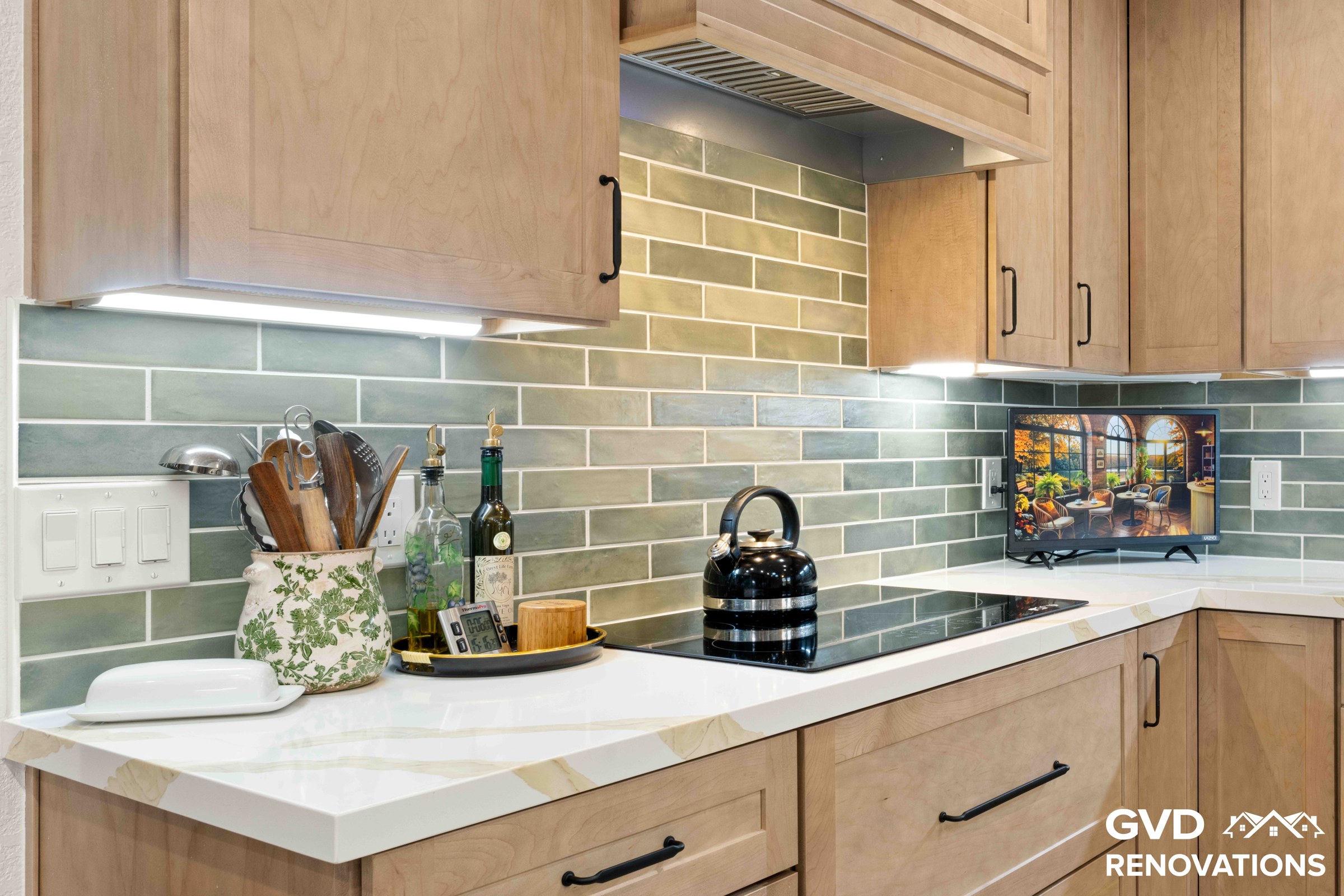 Kitchen cooktop with a stainless steel range hood, sage green subway tile backsplash and under-cabinet LED lighting