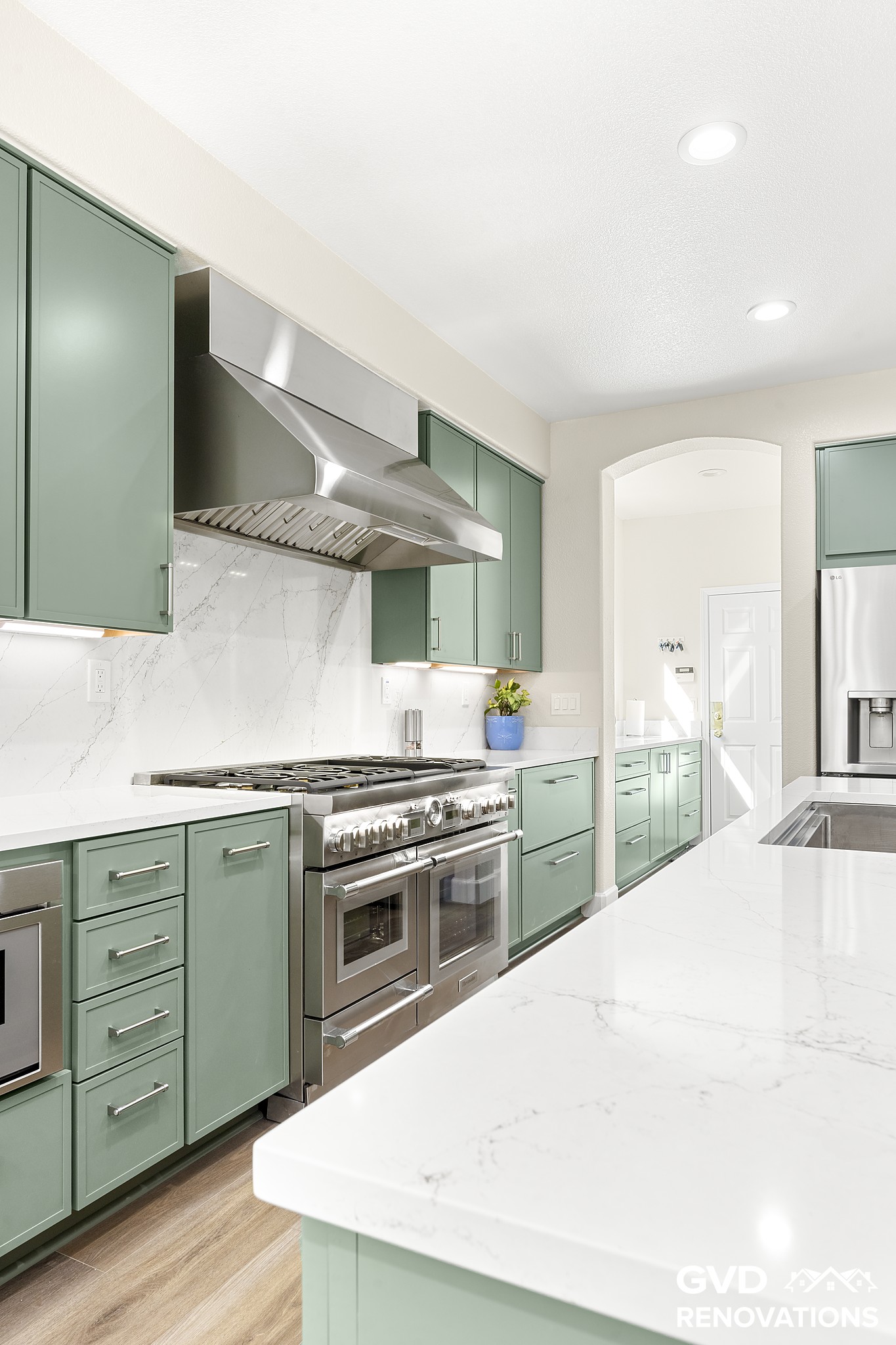 Professional stainless gas range and custom hood framed by sage green cabinetry