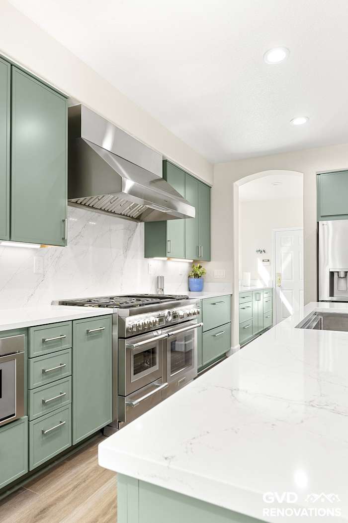 Professional stainless gas range and custom hood framed by sage green cabinetry