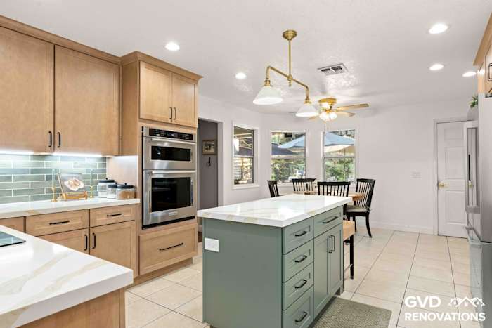 Open kitchen with a sage green island, schoolhouse pendant lights, stainless wall oven and an adjacent dining nook
