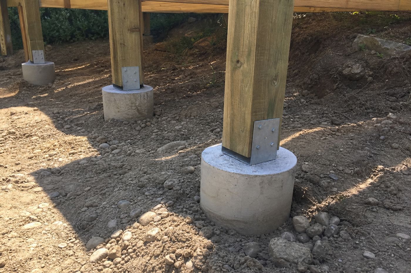 Concrete deck footings with galvanized post-base brackets holding pressure-treated posts