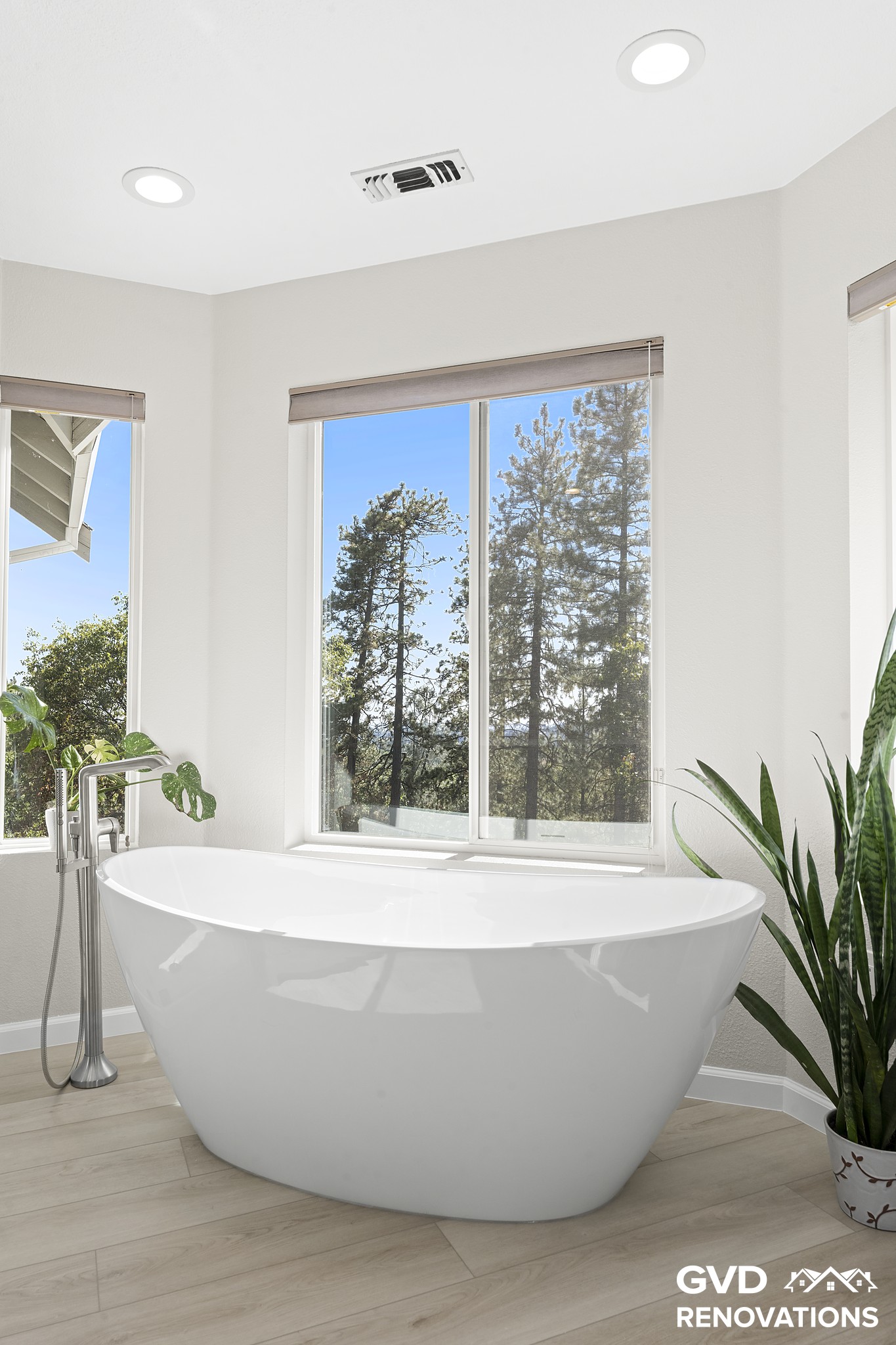 Freestanding soaking tub framed by forest-view windows in the remodeled primary bath