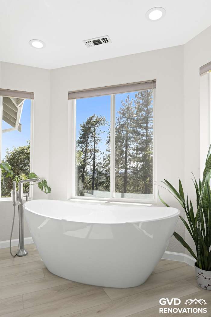 Freestanding soaking tub framed by forest-view windows in the remodeled primary bath