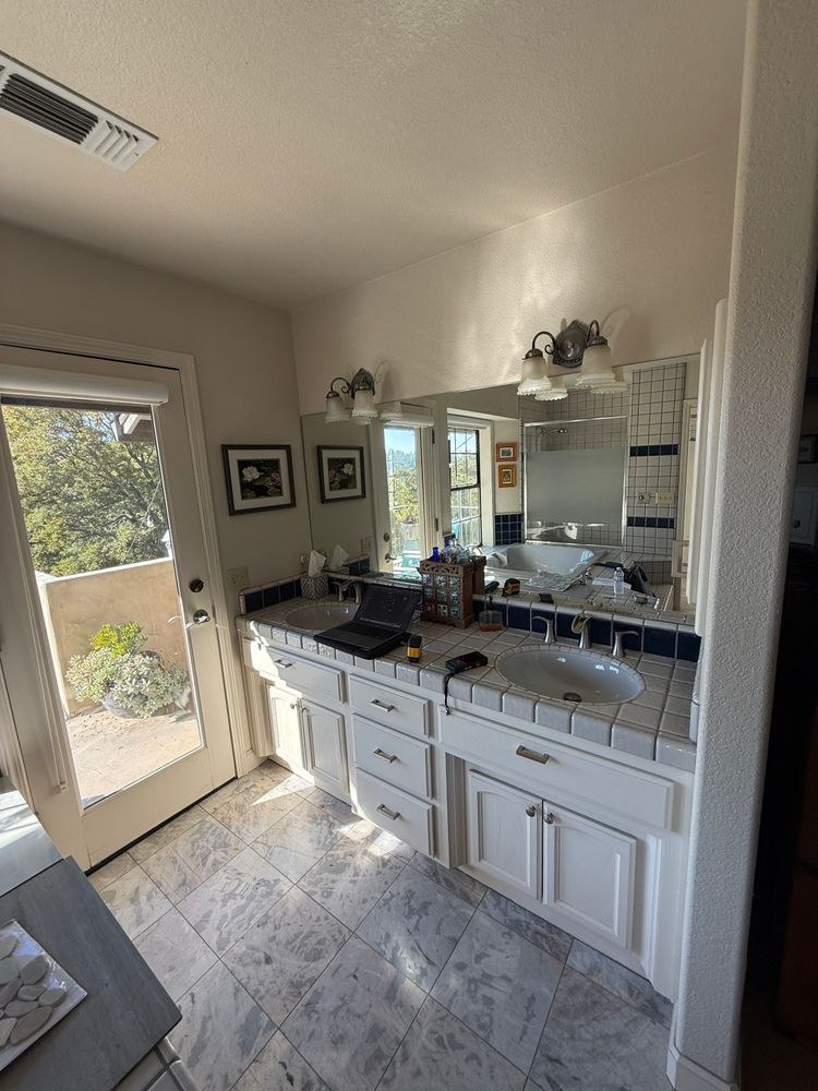 Before: original master bathroom with a white tile-top double vanity, dated fixtures and a marble-tile floor
