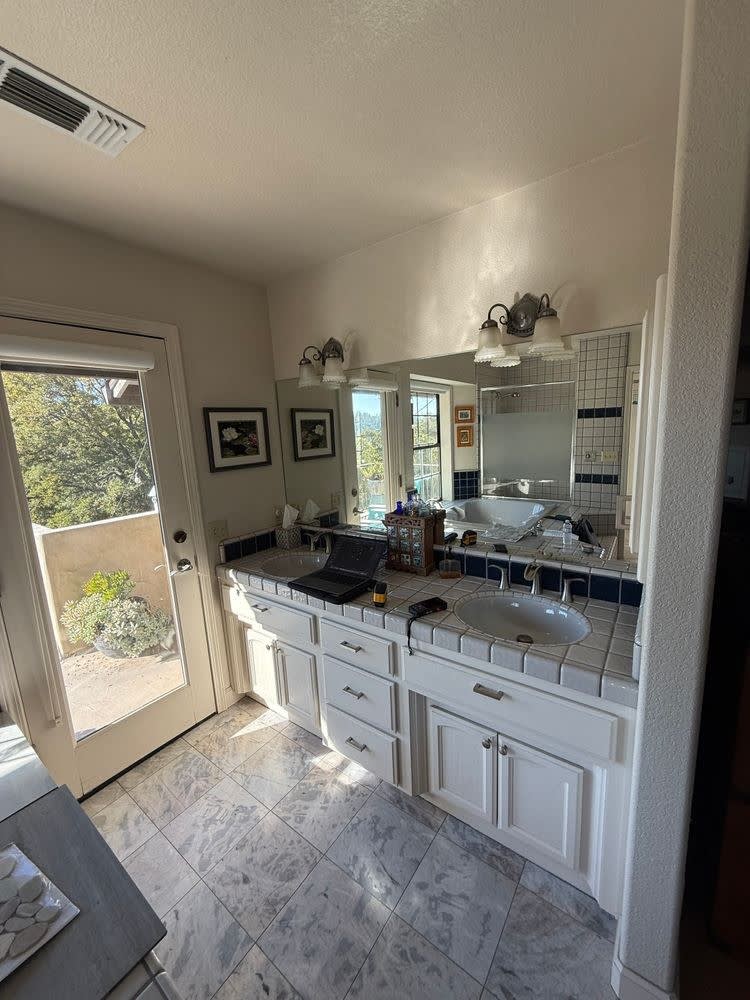 Before: original master bathroom with a white tile-top double vanity, dated fixtures and a marble-tile floor