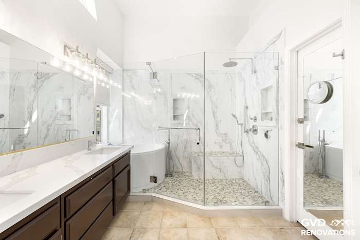 Master bath with a double vanity, freestanding soaking tub and a frameless glass walk-in shower in marble-look tile