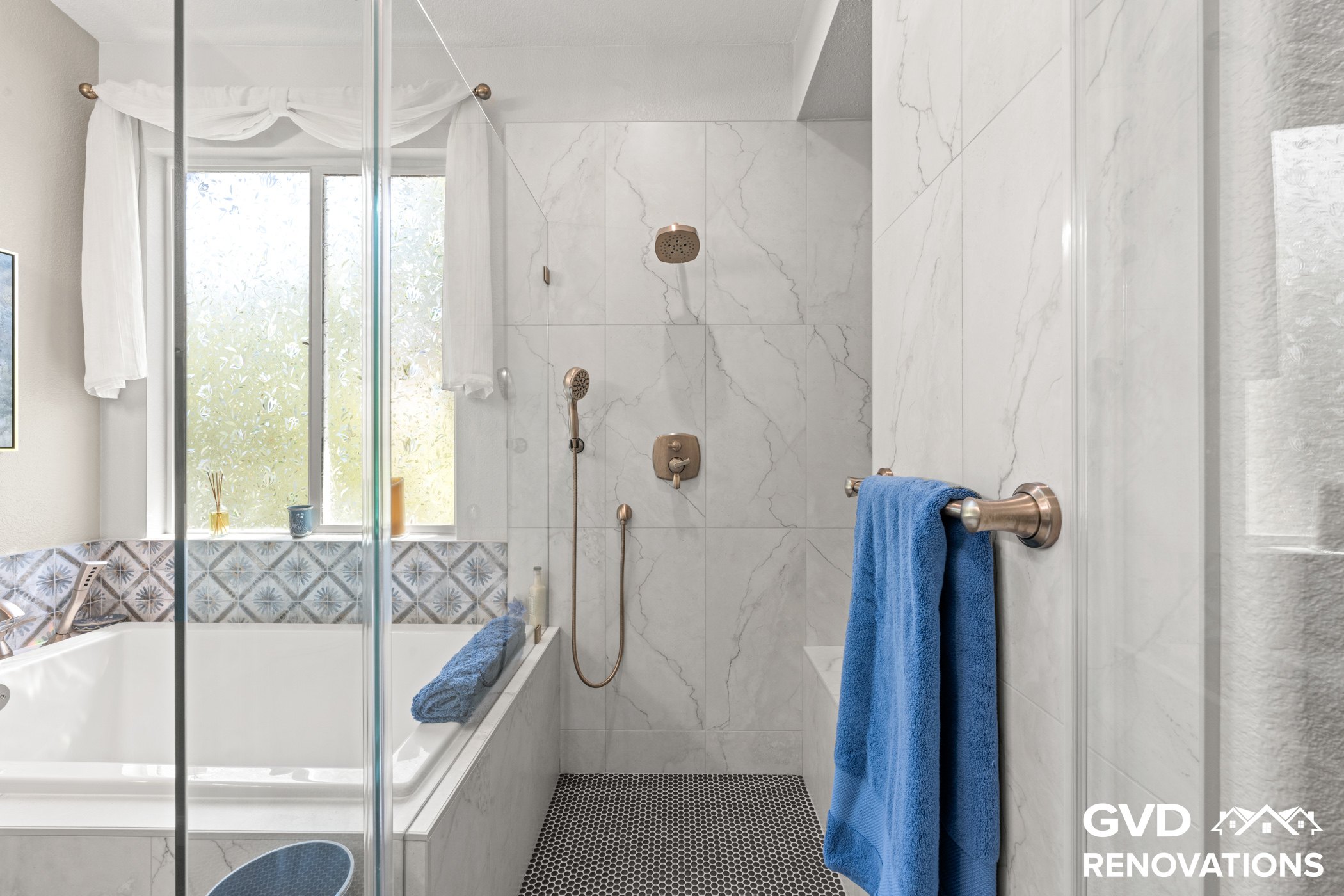 Drop-in soaking tub and frameless glass shower with marble tile and a blue accent band