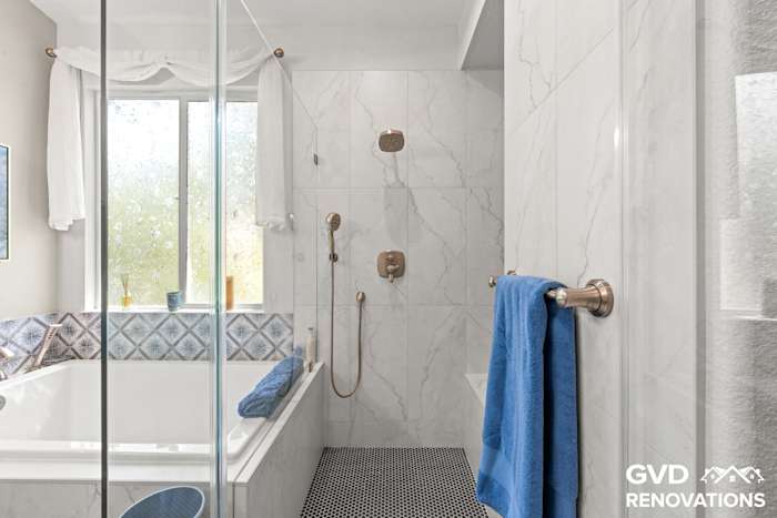 Drop-in soaking tub and frameless glass shower with marble tile and a blue accent band