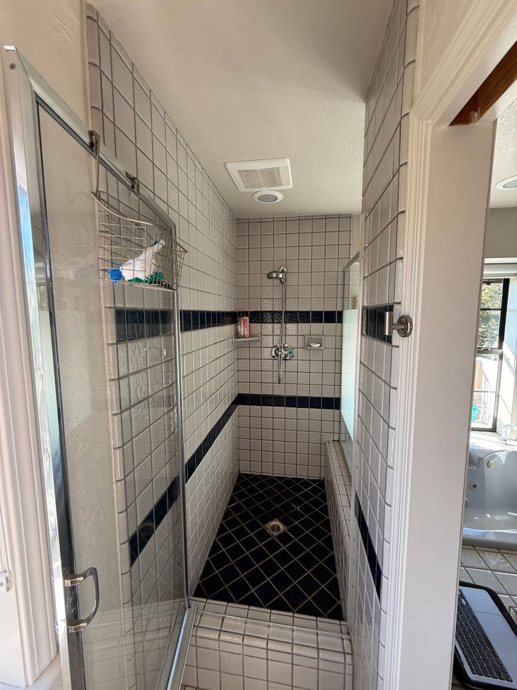 Before: original walk-in shower with white and navy accent tile and a framed glass door
