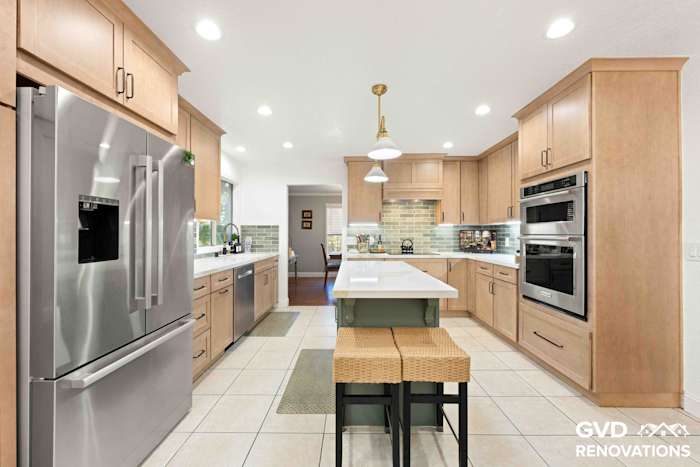 Wide view of the remodeled kitchen with a sage green island, counter seating, brass pendant lights and stainless steel appliances in Rescue, CA