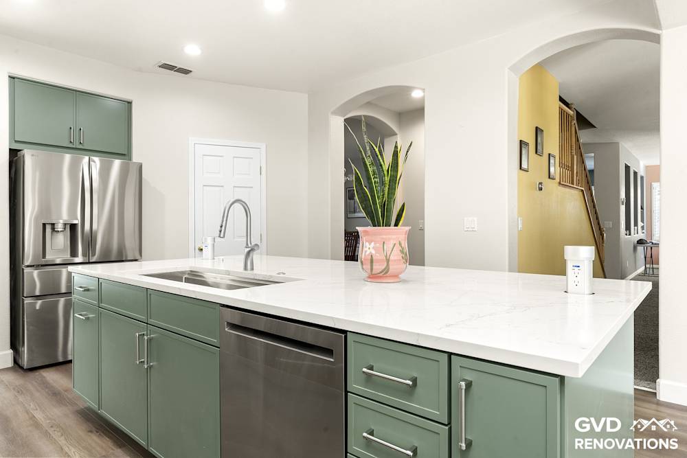 Quartz island with a stainless dishwasher and French-door refrigerator in a sage green kitchen