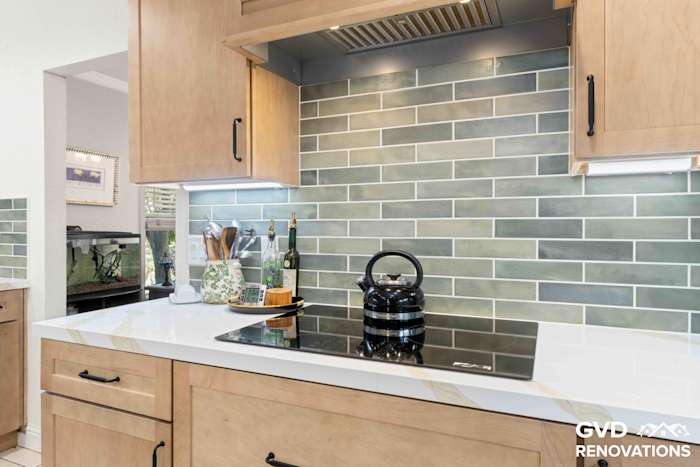 Kitchen island with an electric cooktop beneath a custom wood vent hood, Calacatta quartz countertop and sage green subway tile backsplash