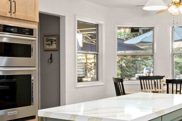 Full kitchen remodel featuring a sage green island, brass schoolhouse pendant lights, built-in wall ovens and recessed lighting