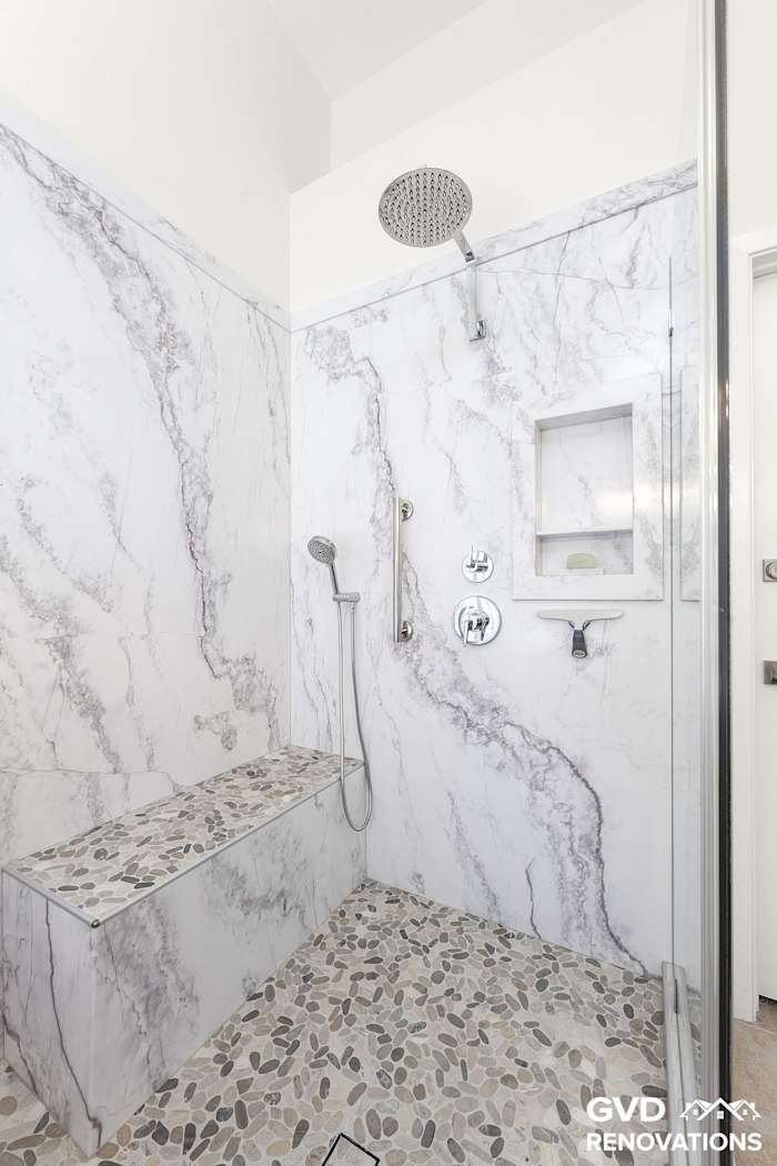 Rainfall shower head and handheld sprayer on large-format marble-look shower walls