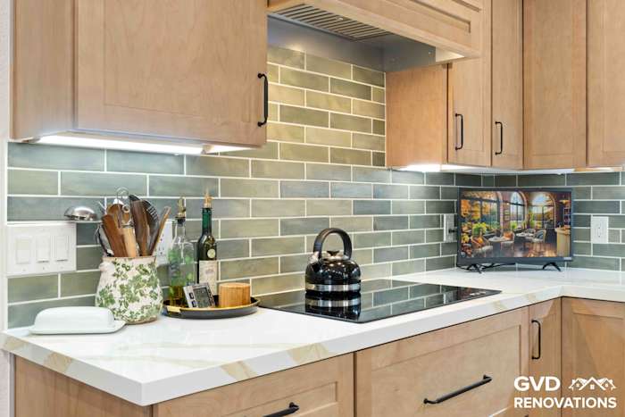 Maple cabinet counter with green subway tile backsplash, under-cabinet lighting and a Calacatta quartz surface