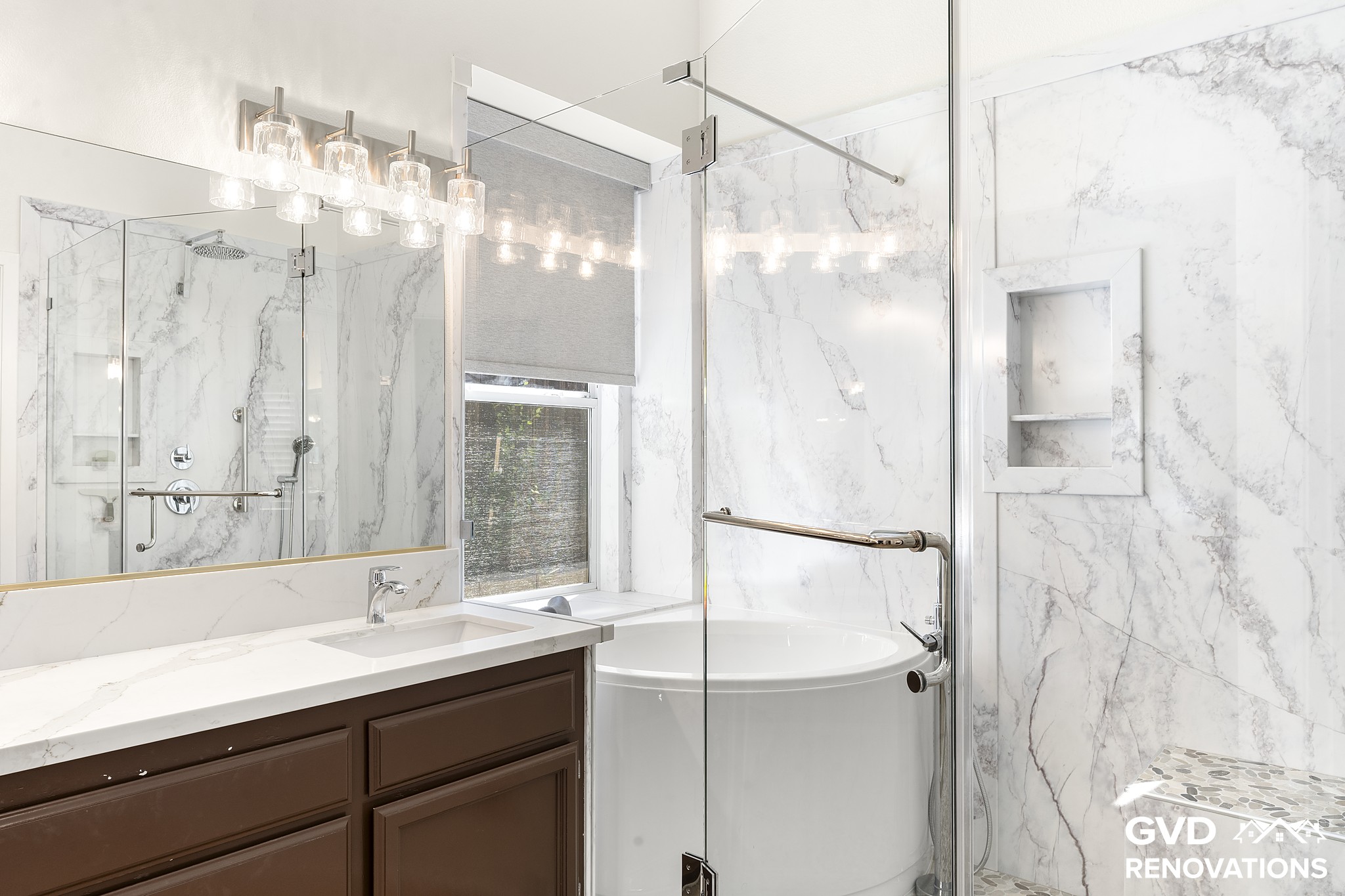 Dark-wood double vanity with a marble-look quartz countertop beside a freestanding soaking tub