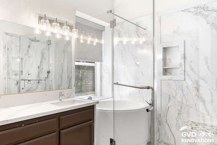 Dark-wood double vanity with a marble-look quartz countertop beside a freestanding soaking tub