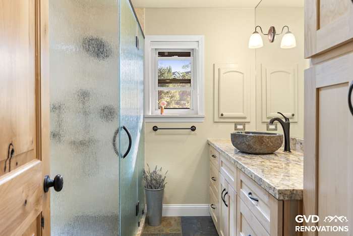 Remodeled guest bathroom in El Dorado Hills with a maple vanity, a stone vessel sink and a glass walk-in shower with slate flooring