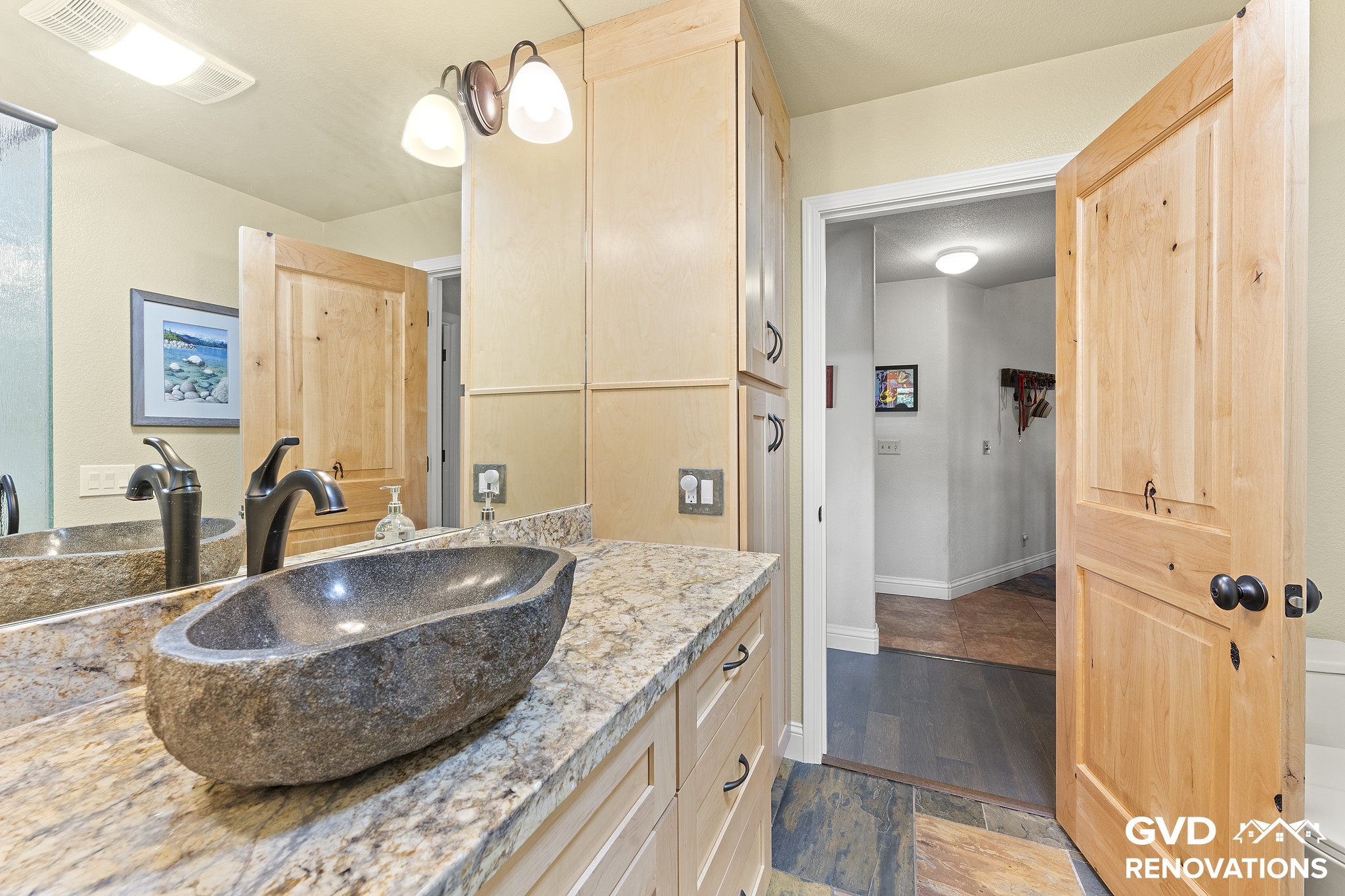 Stone vessel sink on a granite countertop with a matte-black faucet and maple cabinetry