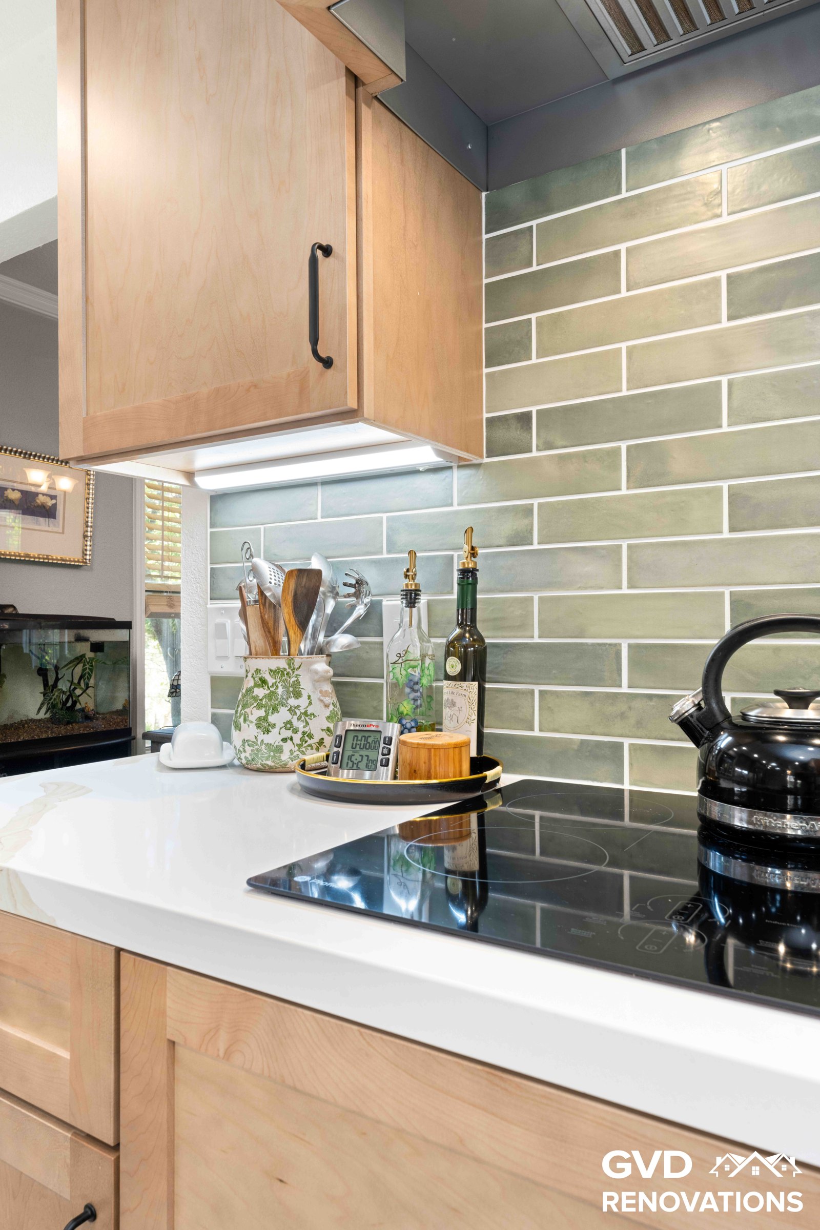 Black cooktop set into a Calacatta quartz countertop with a sage green glass subway tile backsplash