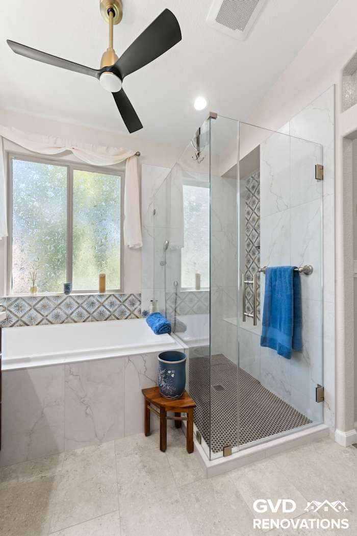 Soaking tub beside a frameless glass shower with a tiled bench