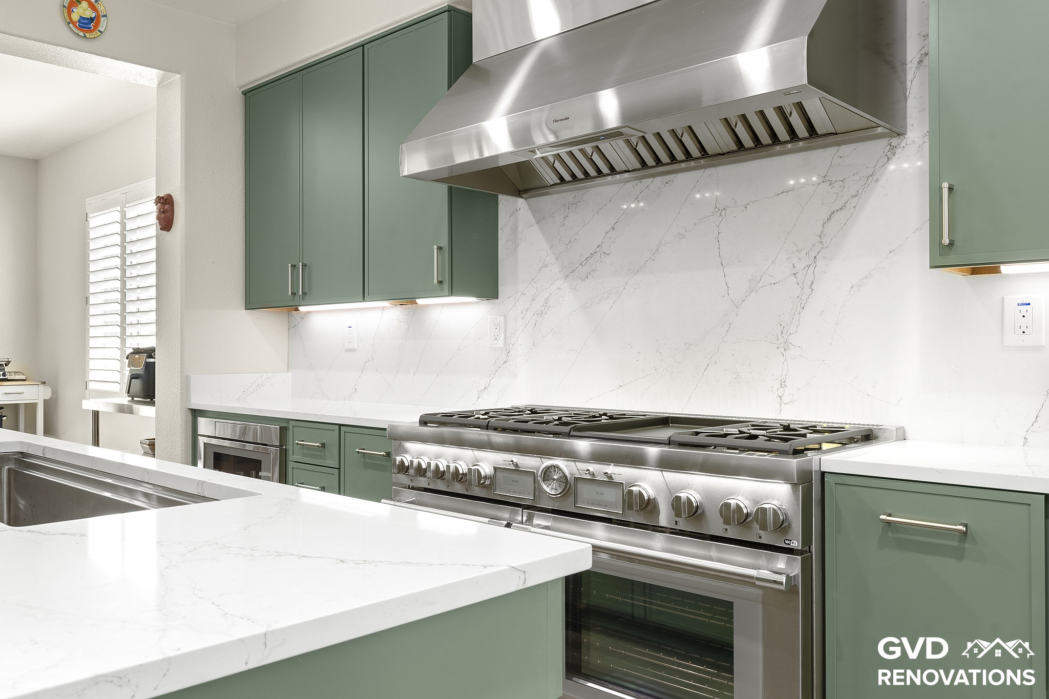 Professional gas range beneath a custom stainless hood with a full-height quartz slab backsplash