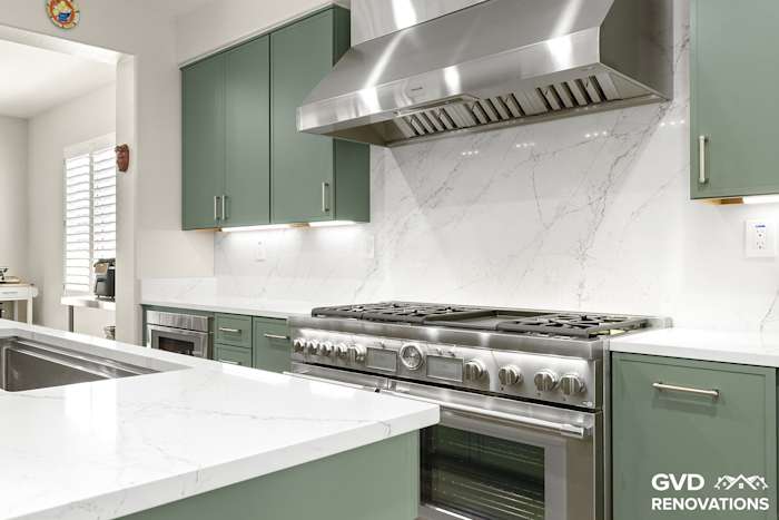 Professional gas range beneath a custom stainless hood with a full-height quartz slab backsplash
