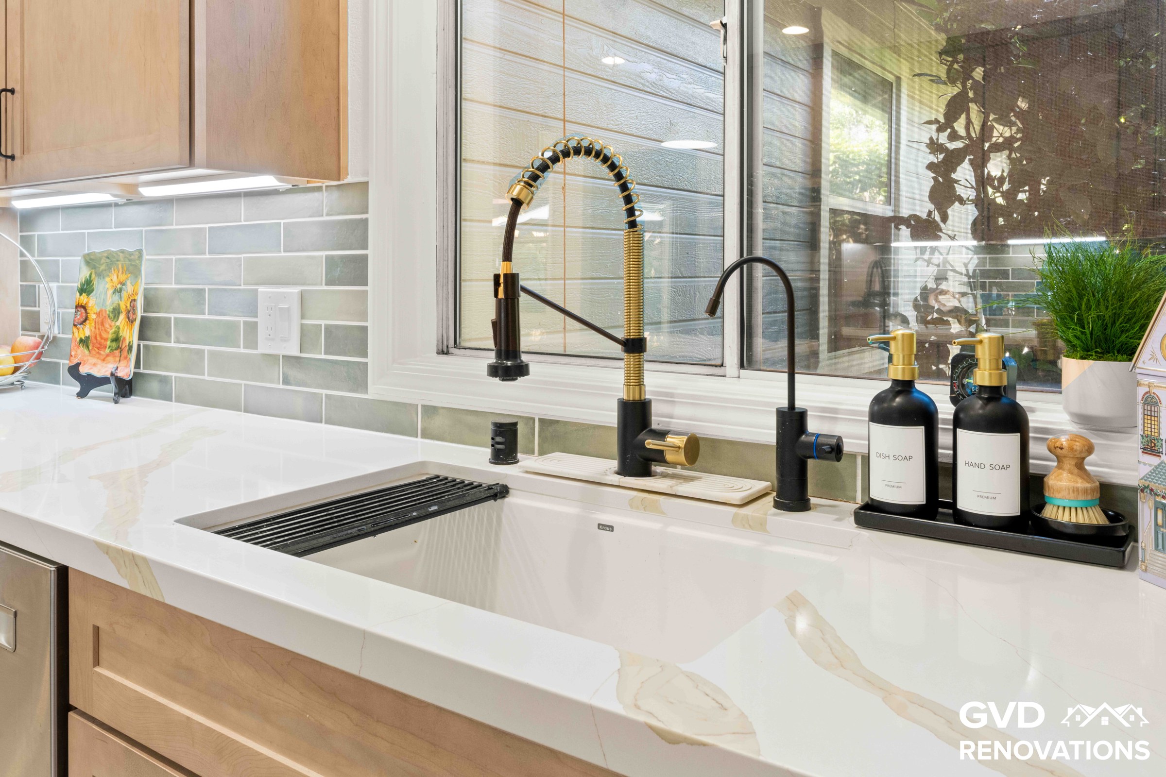 Corner kitchen sink with a black and brass faucet, Calacatta quartz counters and a large picture window