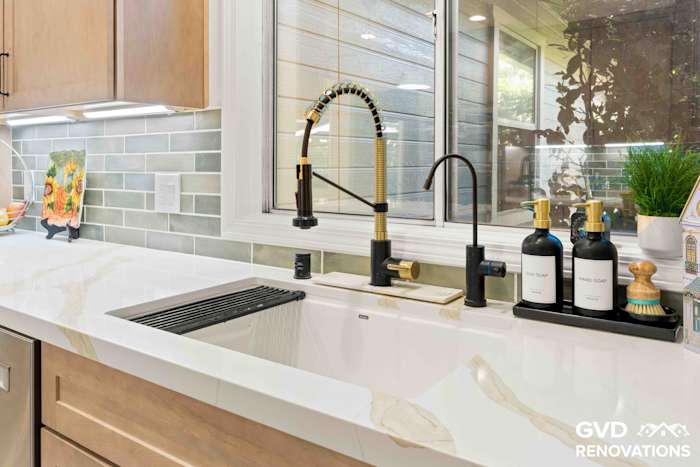 Corner kitchen sink with a black and brass faucet, Calacatta quartz counters and a large picture window