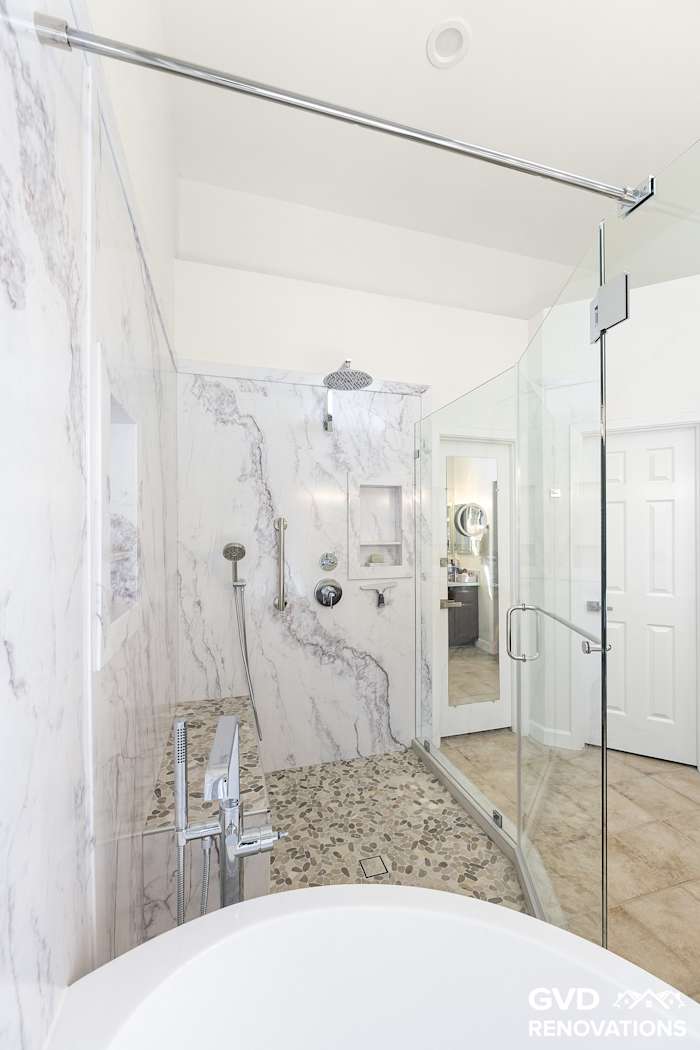 Frameless glass enclosure wrapping the walk-in shower and freestanding tub wet room