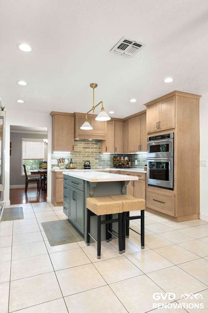 Bright remodeled kitchen with a sage green island, brass pendant lights and stainless steel wall ovens