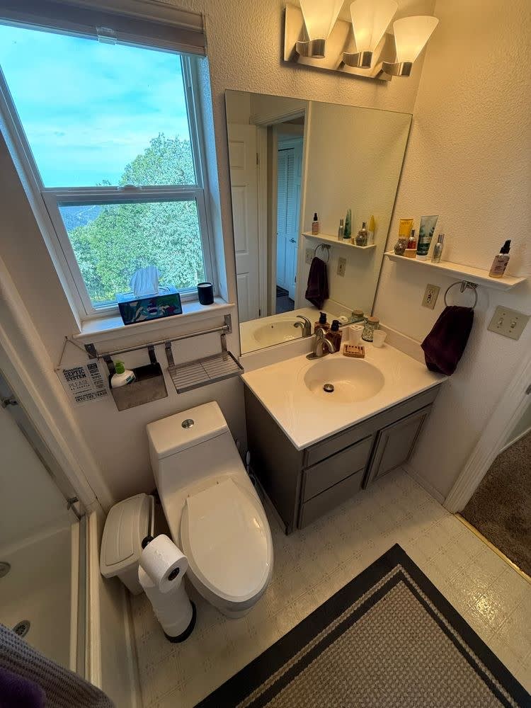 Before: original grey single vanity with a large mirror and vanity lights beneath the window