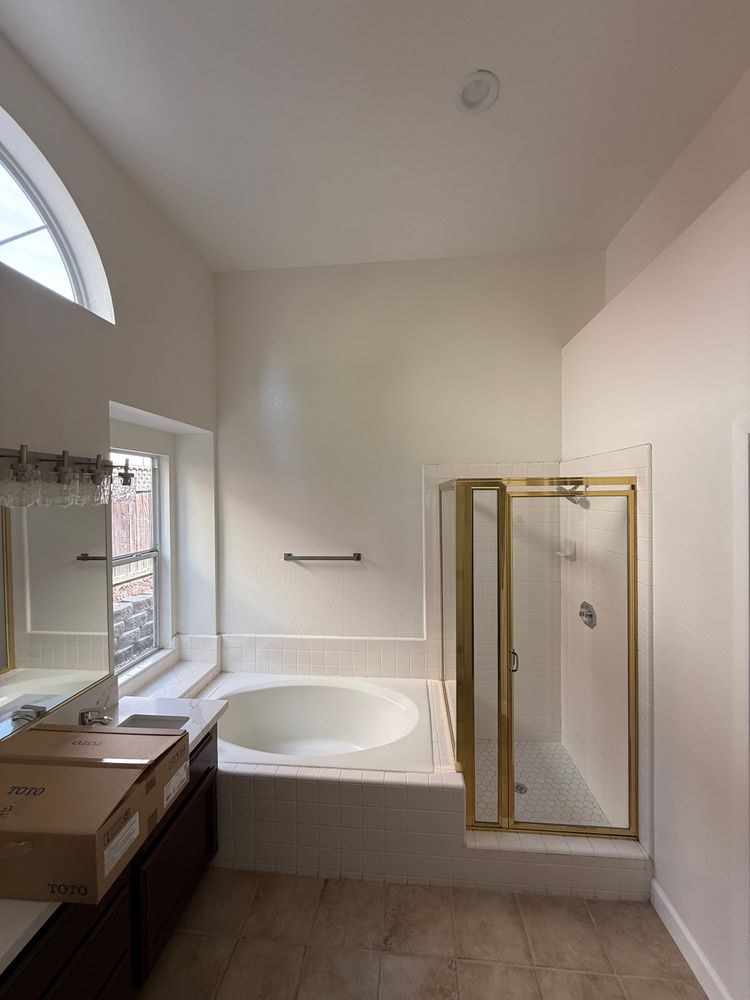 Before: original master bathroom with a dark-wood double vanity, a drop-in oval tub and a gold-framed shower beneath a tall arched window