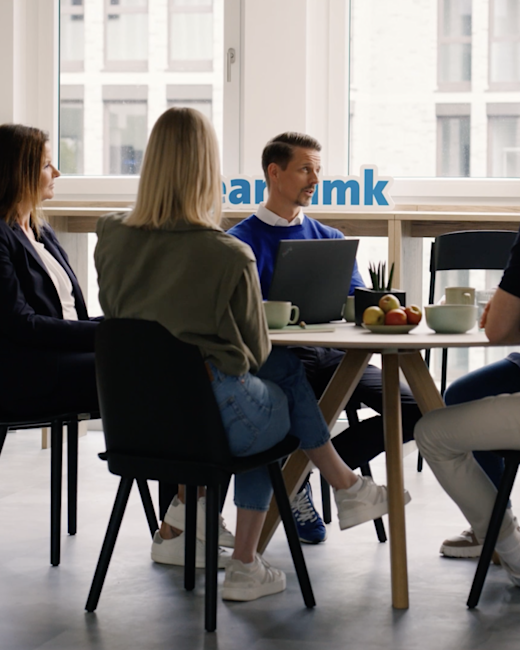 Case | DMK | Gallery 2 | Bild 4 Drei Menschen sitzen an einem runden Tisch auf dem Obst und Tassen stehen