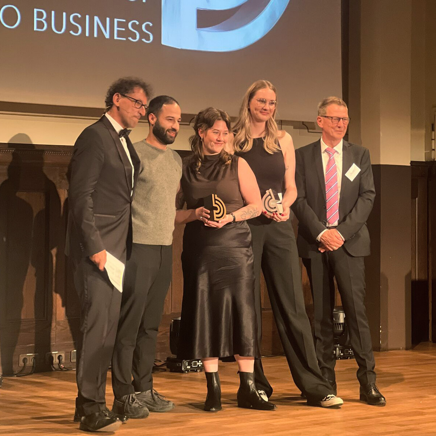 5 Menschen stehen auf einer Bühne, 2 Frauen halten je einen Preis in den Händen