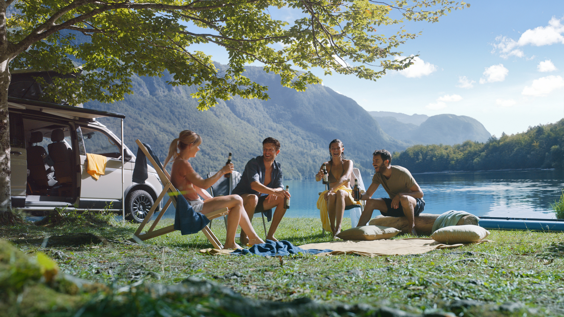 Zwei Pärchen campen vor einem Bergsee und trinken Bitburger aus der Flasche