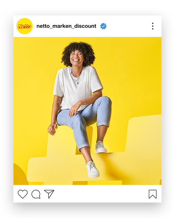 Auf einem gelben Hintergrund steht der Name „Netto“ in ca. 160cm hohen Buchstaben. Auf einem„t“ sitzt eine Frau