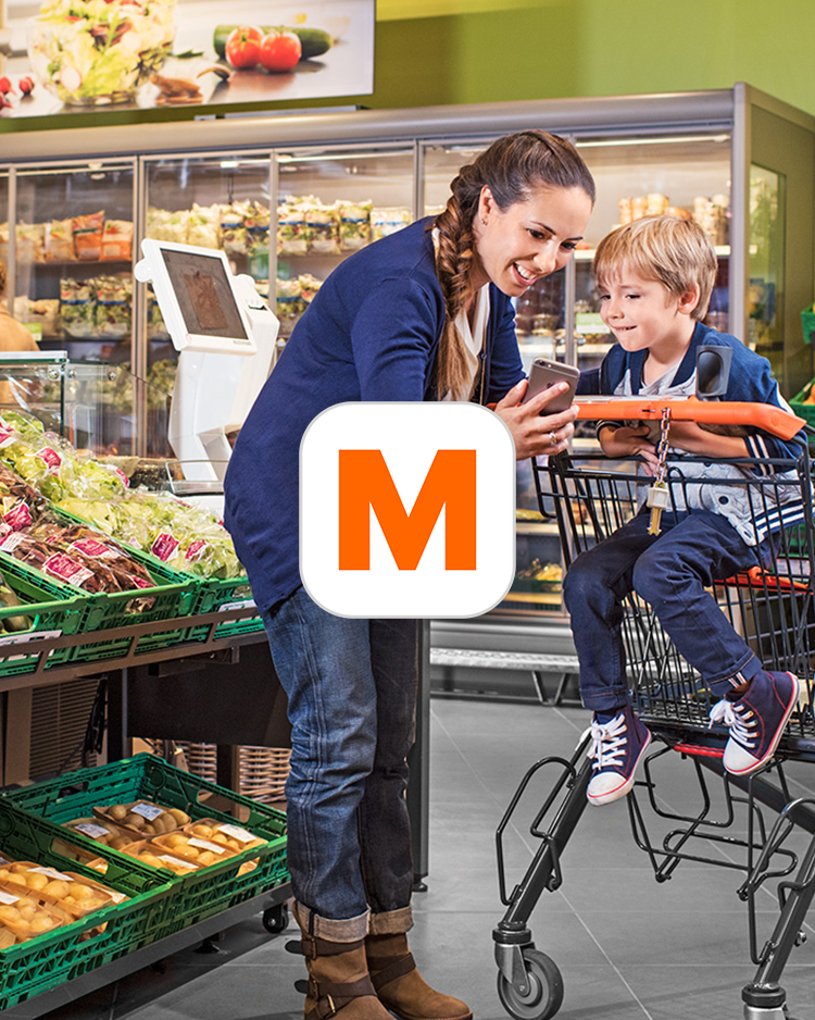In einem Migros Supermarkt in der Gemüseabteilung zeigt eine Mutter ihrem Sohn etwas auf einem Handy