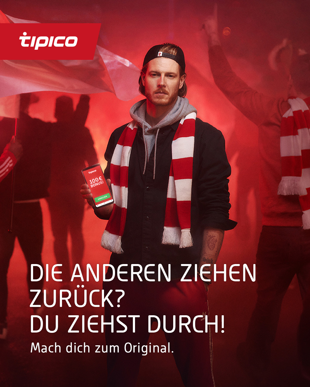 Ein Mann mit  rot weißem Schal und Handy in der Hand steht vor einem unscharfen rotem Hintergrund in weißer Schrift steht vor dem Bild „ DIE ANDEREN ZIEHEN ZURÜCK? DU ZIEHST DURCH! Mach dich um Original!