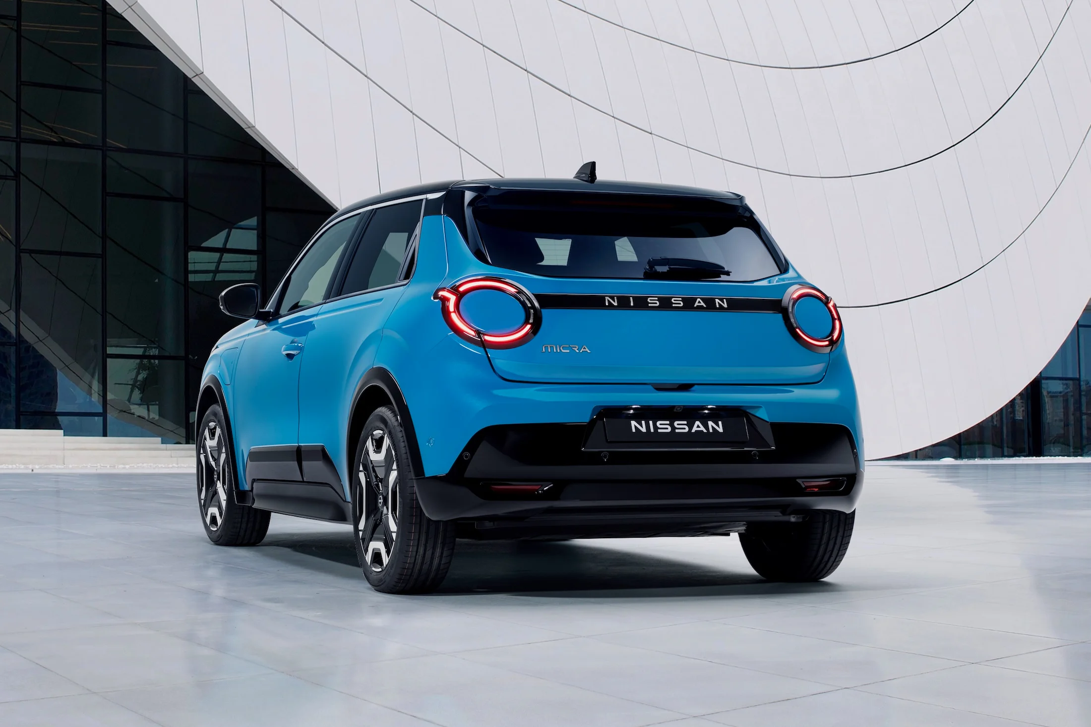 8 view of new Micra in blue gear color in front of a white & blue design architectural building