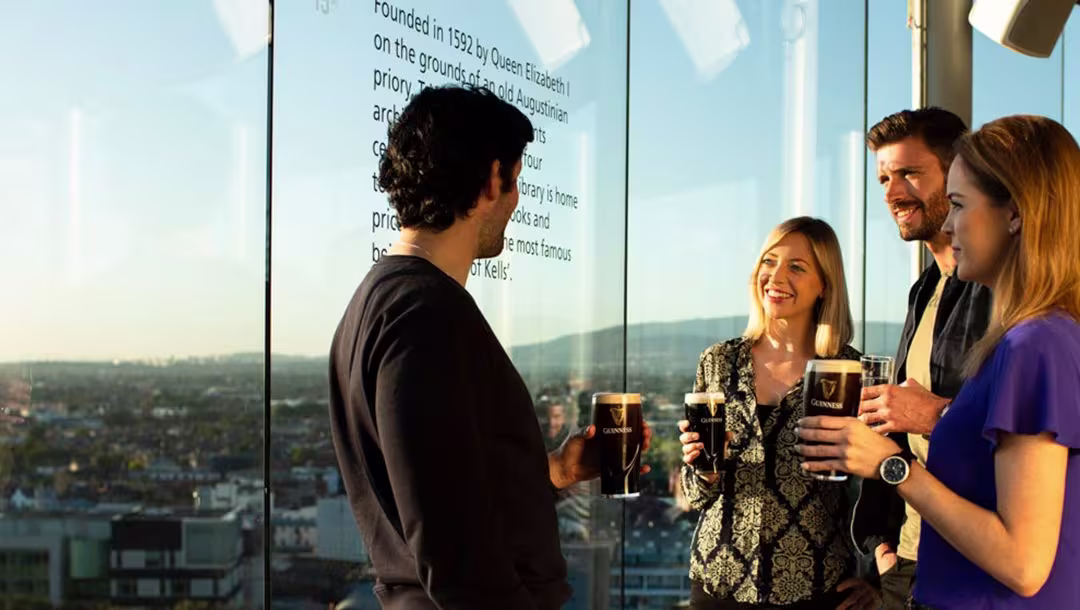 A group of men and women drinking Guinness by a window.