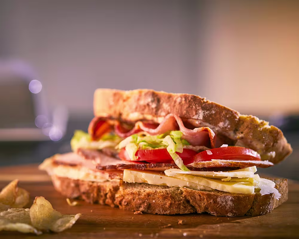 there is a sandwich with ham, lettuce, tomato, and cheese on it